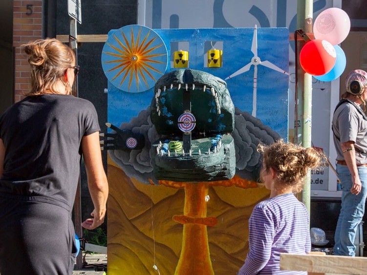 Zwei Menschen werfen Bälle auf die Godzilla-Wurfwand, die das frohnzimmer zum Beispiel bei Stadtteilfesten aufstellt.