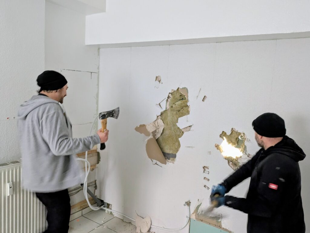 Zwei Menschen reißen beim Umbau des frohnzimmers eine Wand ein.