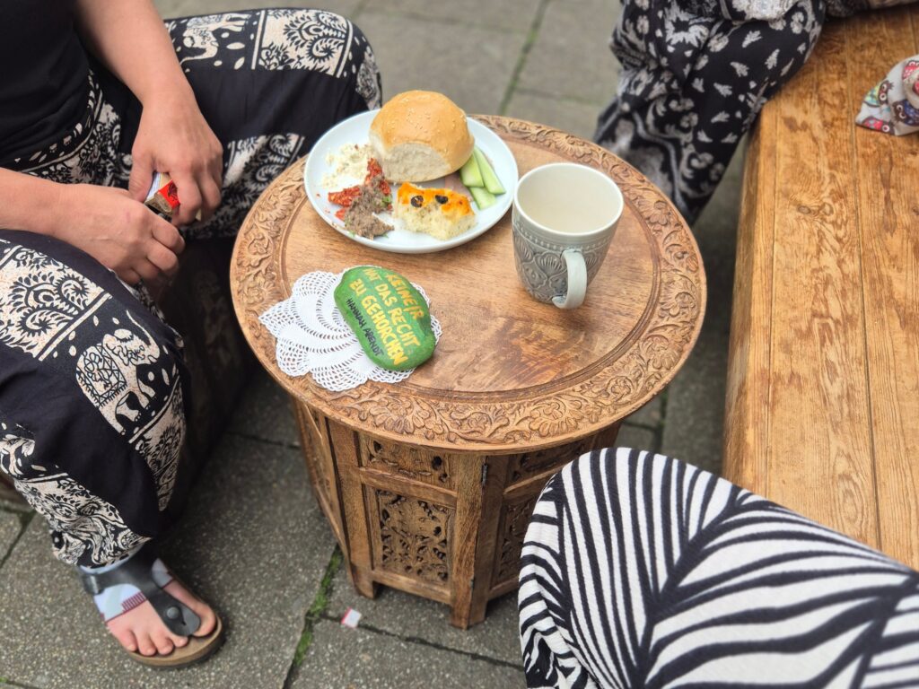 Ein kleiner gedeckter Tisch mit Essen und Getränken, an dem mehrere Menschen sitzen.